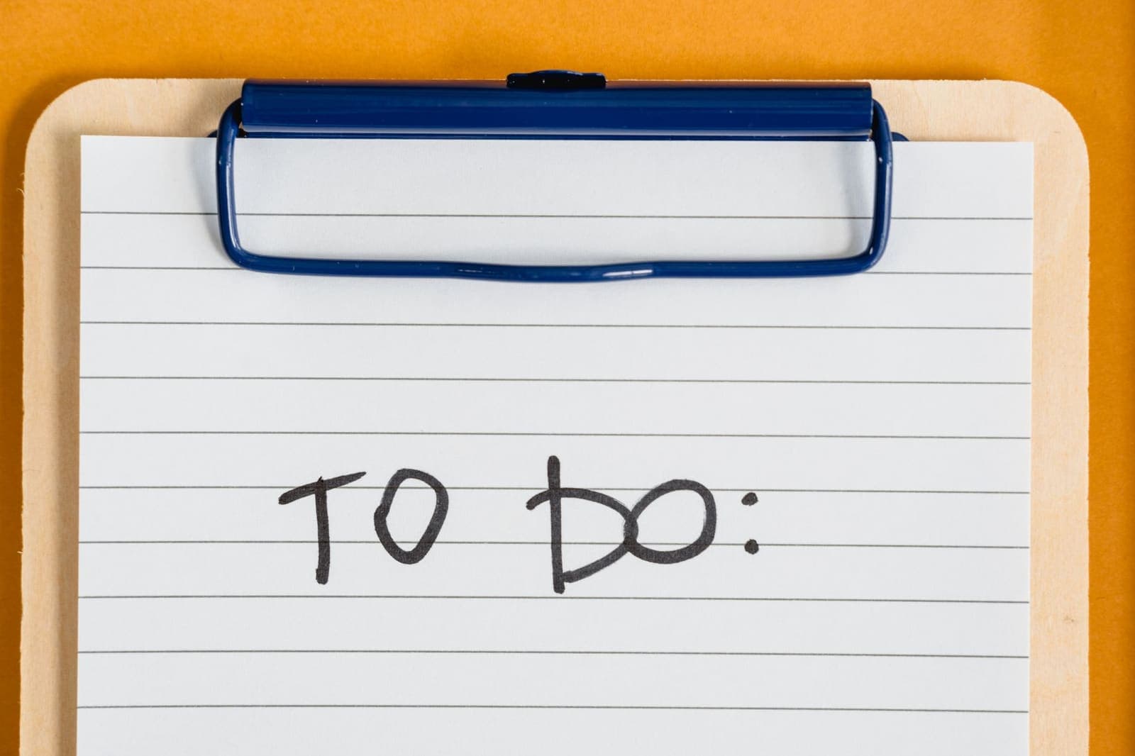 A short handwritten to-do list on a notepad beside a coffee cup on a desk